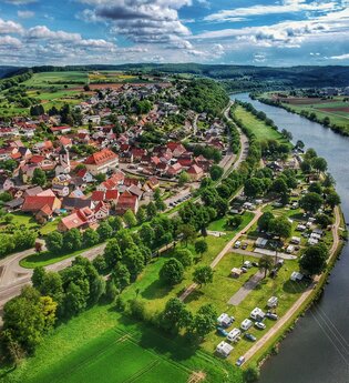 Drohnenaufnahme mit Blick auf einen Fluss (Neckar). Auf der rechten Uferseite sieht man einen Campingplatz und dahinter einen angrenzenden Ort. Binau im Odenwald. | © Fortuna Camping am Neckar