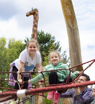 2 Kinder auf einem Klettergerüst. Die Eltern stehen davor. Im Hintergrund ist ein lebensgroße Holzgiraffe. Schwarzach im Odenwald. | © Touristikgemeinschaft Odenwald e.V.