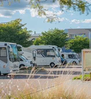 Gepflasterter Stellplatz mit mehreren Wohnmobilen und einer Informationstafel