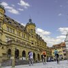 Blick auf den Marktplatz mit Rathaus in Rothenburg o.d.T.  Hier fahren gerade drei Radelnde über das Kopfsteinpflaster.