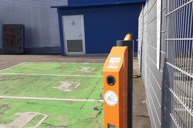 E-Ladesäulen zwischen grüner Parkfläche und Zaun