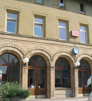 Das Bahnhofsgebäude von außen, hier hängt ein DB-Schild und eine Uhr | © Touristikgemeinschaft Hohenlohe e. V. | Stadt Öhringen