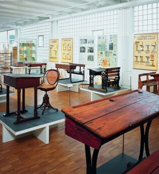Blick in das Schulmuseum der Firma VS in Tauberbischofsheim. Hier sind alte Schulbänke, Tische und Stühle sowie Wandkarten zu sehen. | © Tourismusverband "Liebliches Taubertal" e.V.