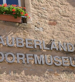 Blick auf den aus einzelnen Metallbuchstaben zusammengesetzen Namen "Tauberländer Dorfmuseum", der auf der Außenseite des Museums angebracht ist. | © Tourist-Info Weikersheim
