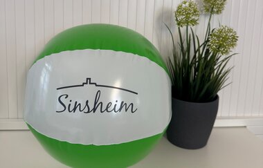 Grün-weißer Wasserball mit der Aufschrift "Sinsheim" vor weißer Wand und grüner Topfpflanze | © Stadt Sinsheim