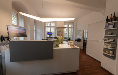 Beleuchtete Empfangstheke der Touristinfo mit Schreibtischen und Schränken
