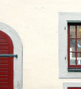 Eingangstüre zur Touristinformation aus dunkelrot gestrichenem Holz, rechts daneben zwei, dunkelrot gestrichene Sprossenfenstertüre, | © Petra Natzkowski