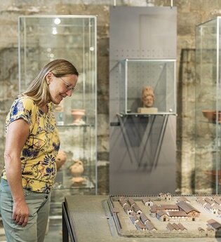 Eine Frau steht vor einer Vitrine mit römischen Funden | © Touristikgemeinschaft Hohenlohe e. V. | Barbara Wagner Fotografie