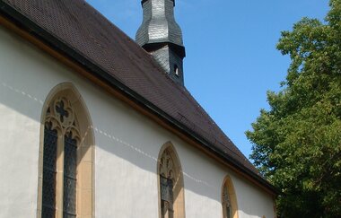 Die Kapelle hat einen langen Turm und ist von einem Baum umgeben
