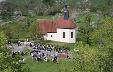 Vor der Kapelle stehen Personen und Reiter